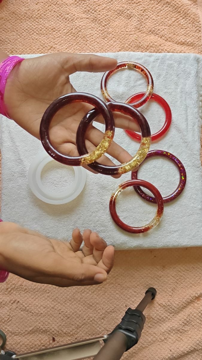 Hands holding freshly made resin bangles beside their moulds